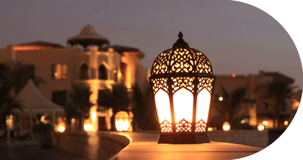 a lantern lit on during the night, with a mosque in the background