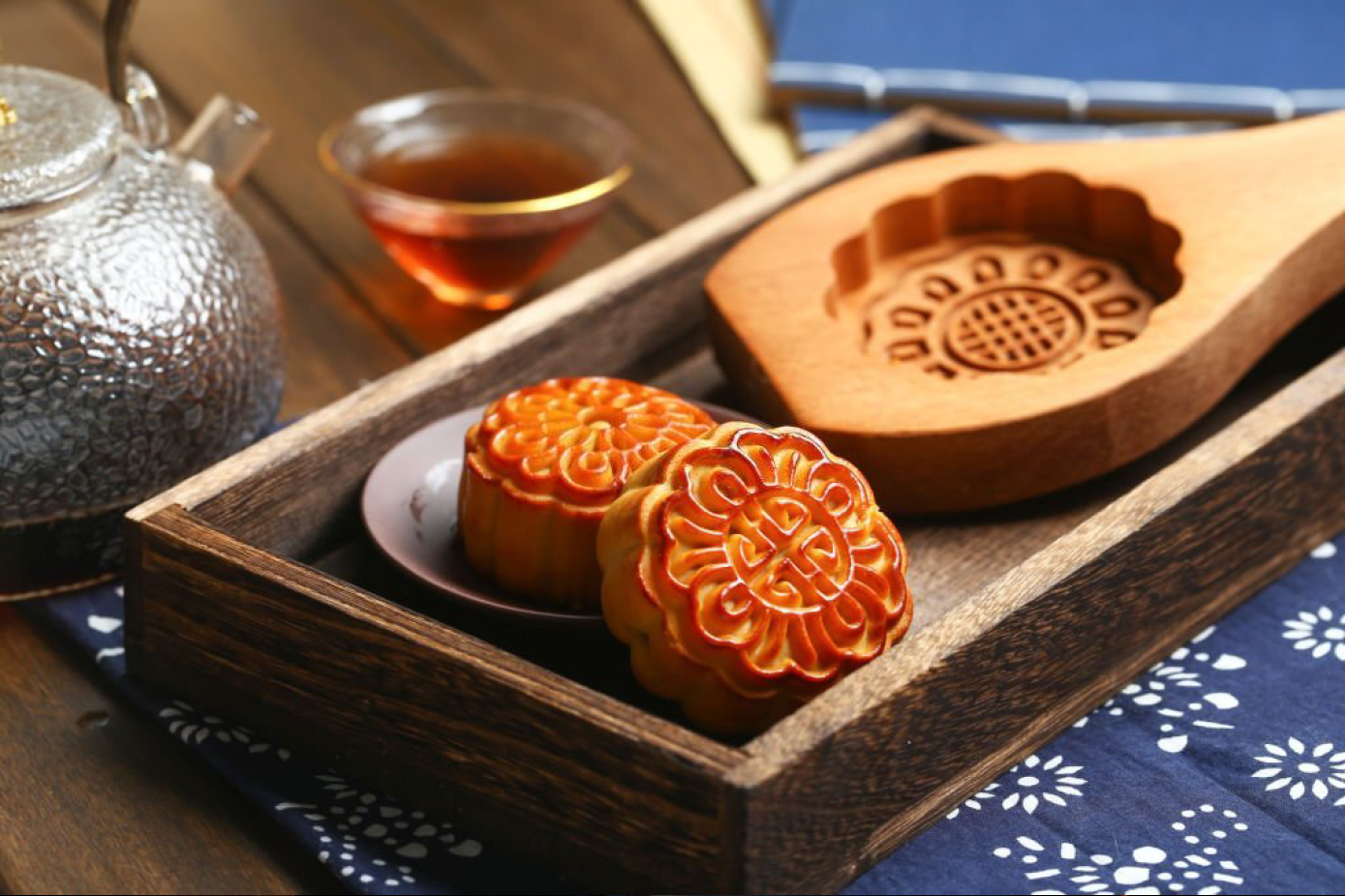 a table with a tray with 2 mooncakes, a mooncake mold and a teapot with a cup of tea on the side