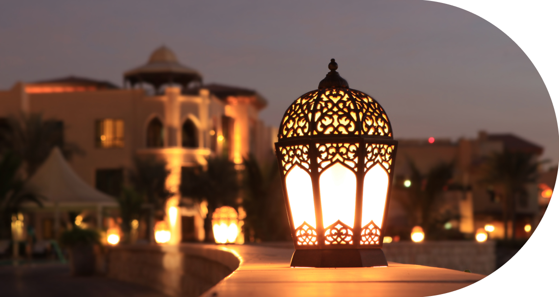 a lantern lit on during the night, with a mosque in the background